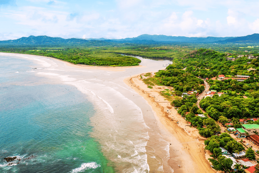 An aerial shot of the beach in Tamarindo showing blue-green water, golden sand, and green trees.